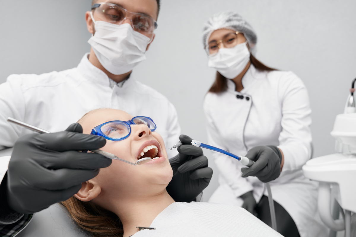 Girl lying on dentist chair while doctor curing teeth